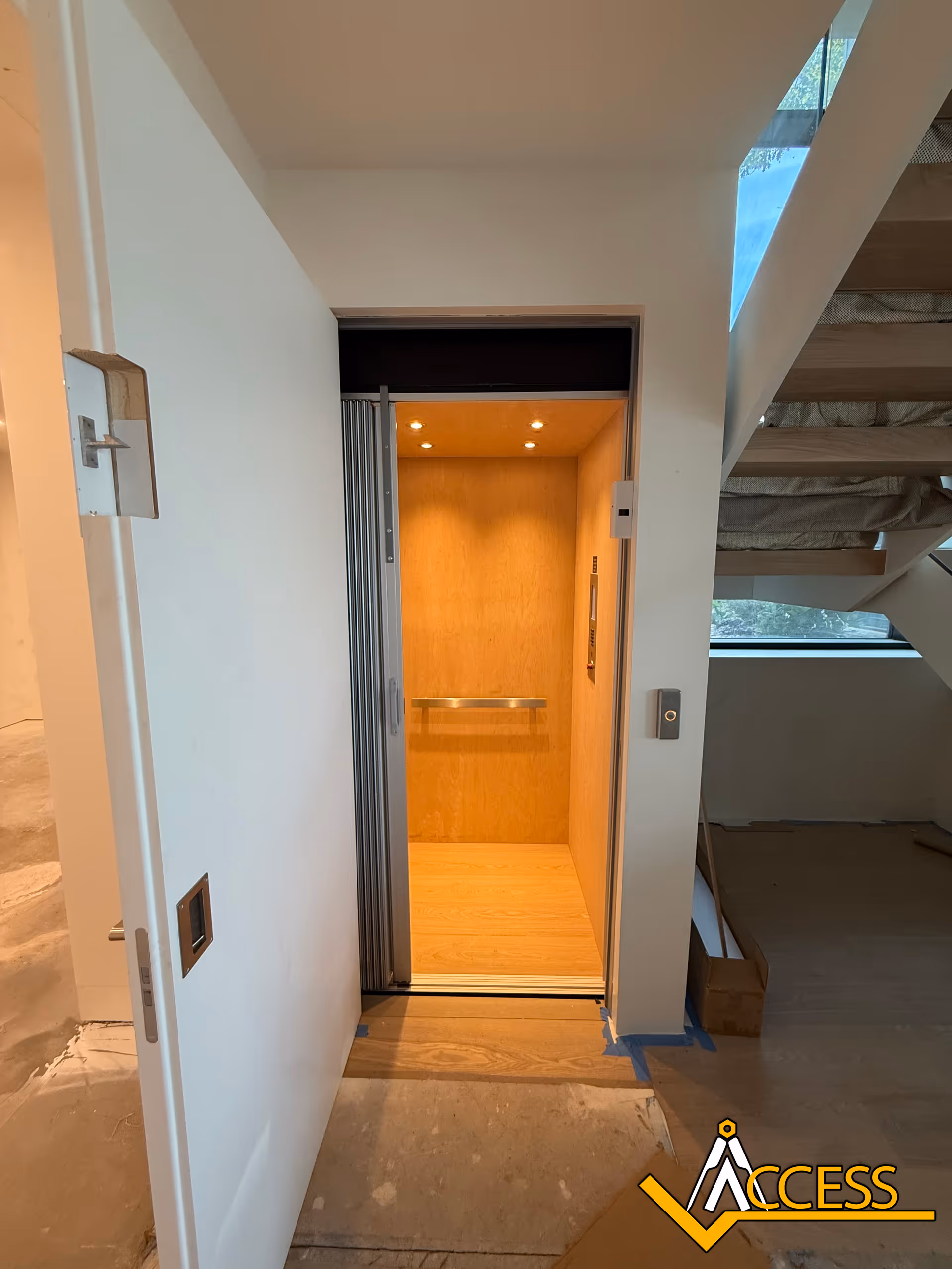 An elevator car with wooden panels is open beside a stairwell in a building.