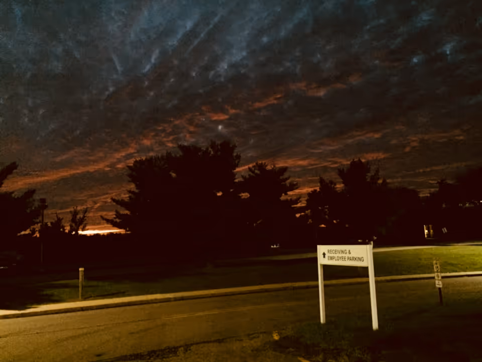 Dusk outdoor parking area with trees and a sign reading Receiving and Employee Parking.