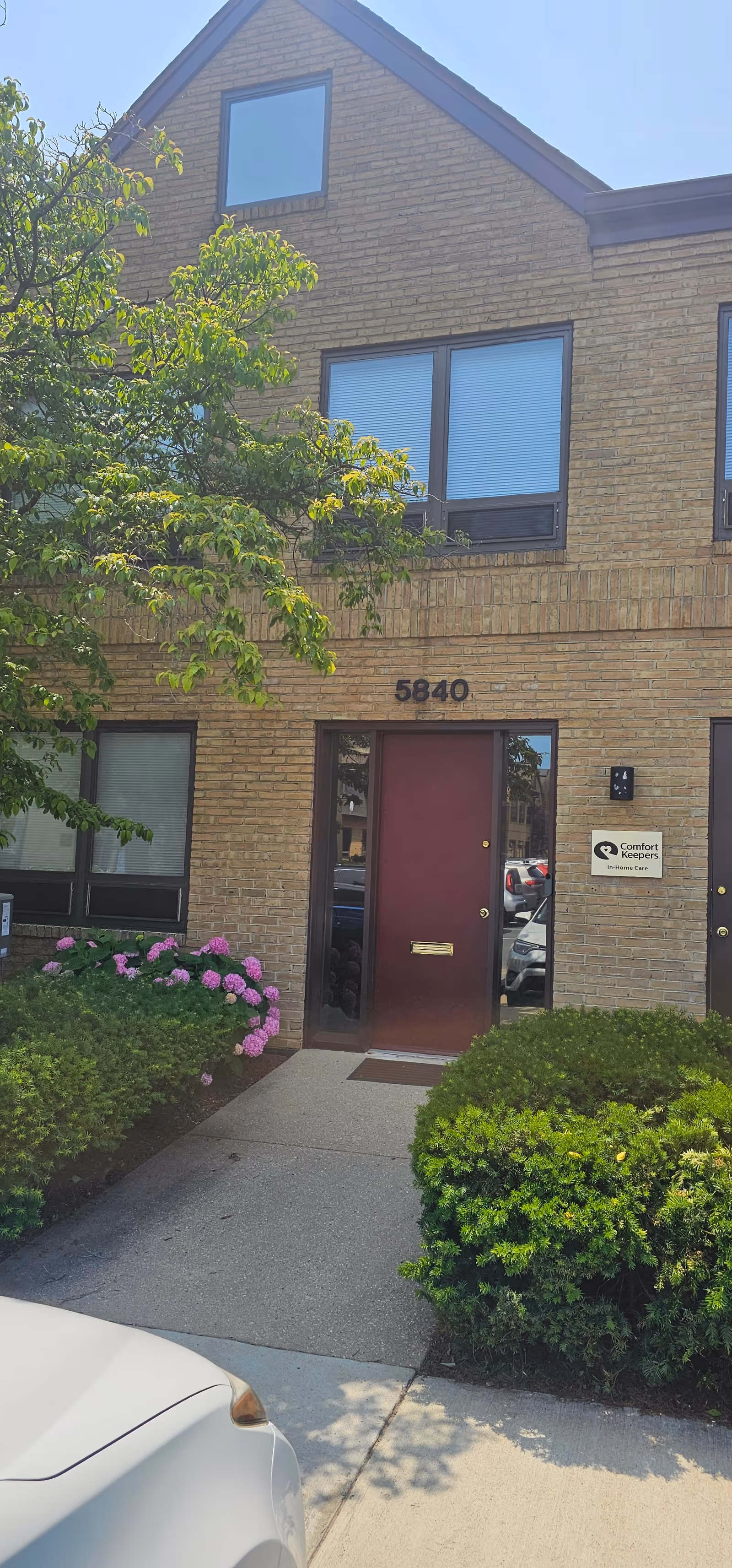 Brick building entrance with a red door, greenery, and the Comfort Keepers sign.