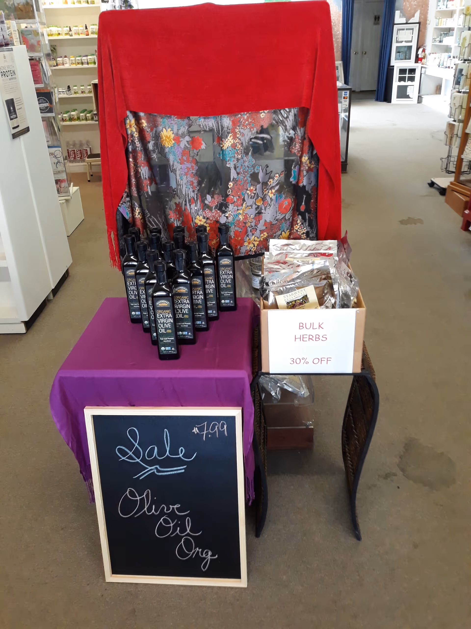 Indoor shop display featuring olive oil bottles, bulk herbs, and a sale sign.