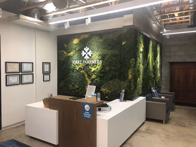 Reception desk in a modern lobby with a moss wall featuring Care Partners logo and seating.