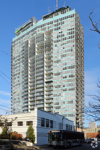 Tall modern high rise with numerous balconies atop a white base building on a city street.
