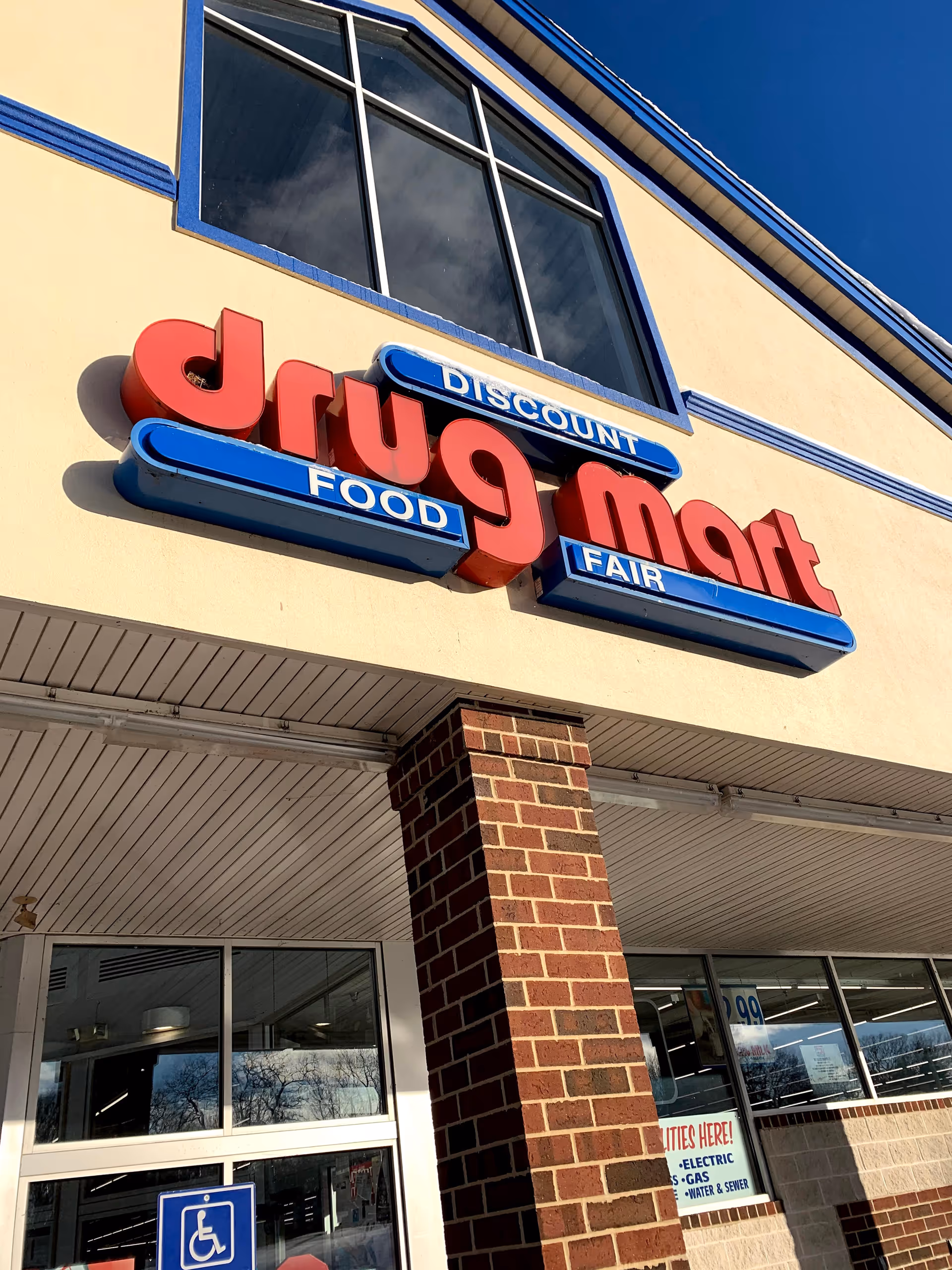 Exterior of Discount Drug Mart storefront with red sign and blue accents under a clear sky.