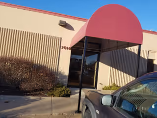 Exterior view of a building entrance with a rounded red awning and a parked car.