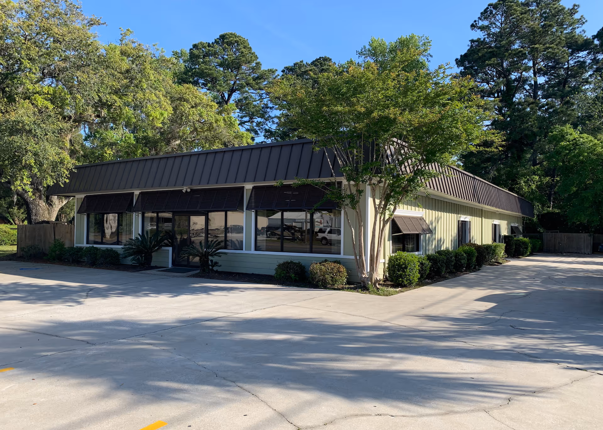Exterior view of a single-story building with large windows, awnings, and trees.