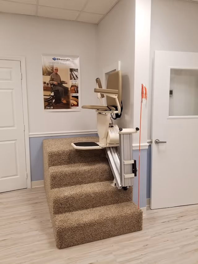 Stair lift chair installed on carpeted steps in a clean facility hallway.