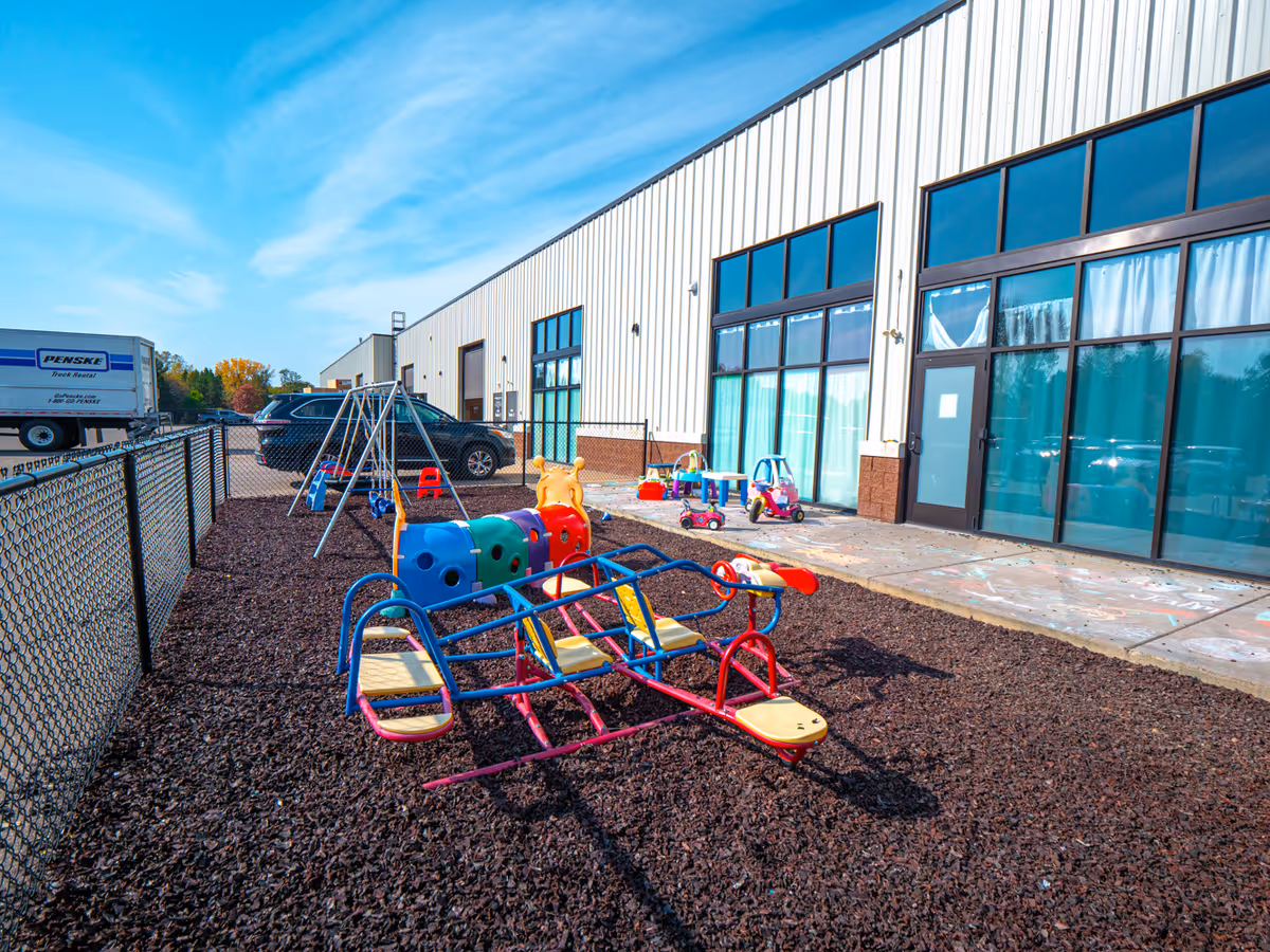Outdoor playground area with colorful equipment beside a modern building's glass entrance.