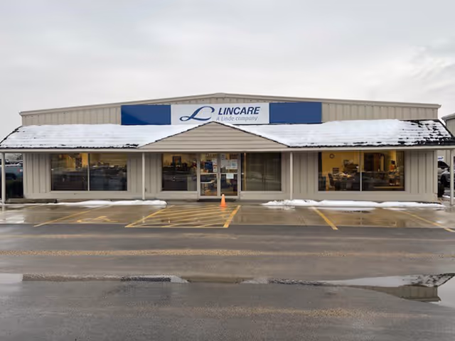 Single-story storefront with a blue Lincare sign, glass doors, windows, and snow on the roof.