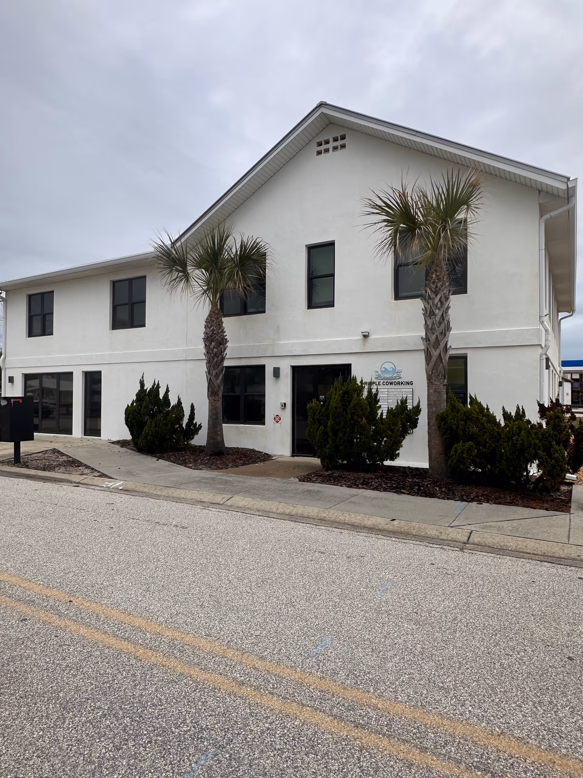 Front view of a white two-story facility with palm trees and shrubs.
