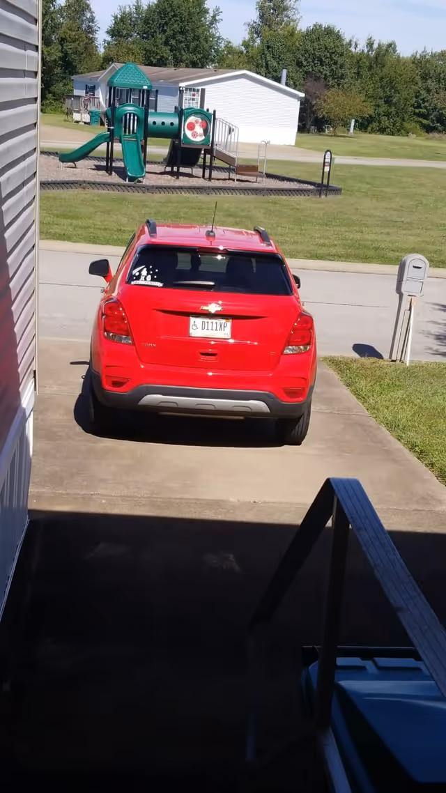 Red SUV parked in driveway with a playground and white building in background.