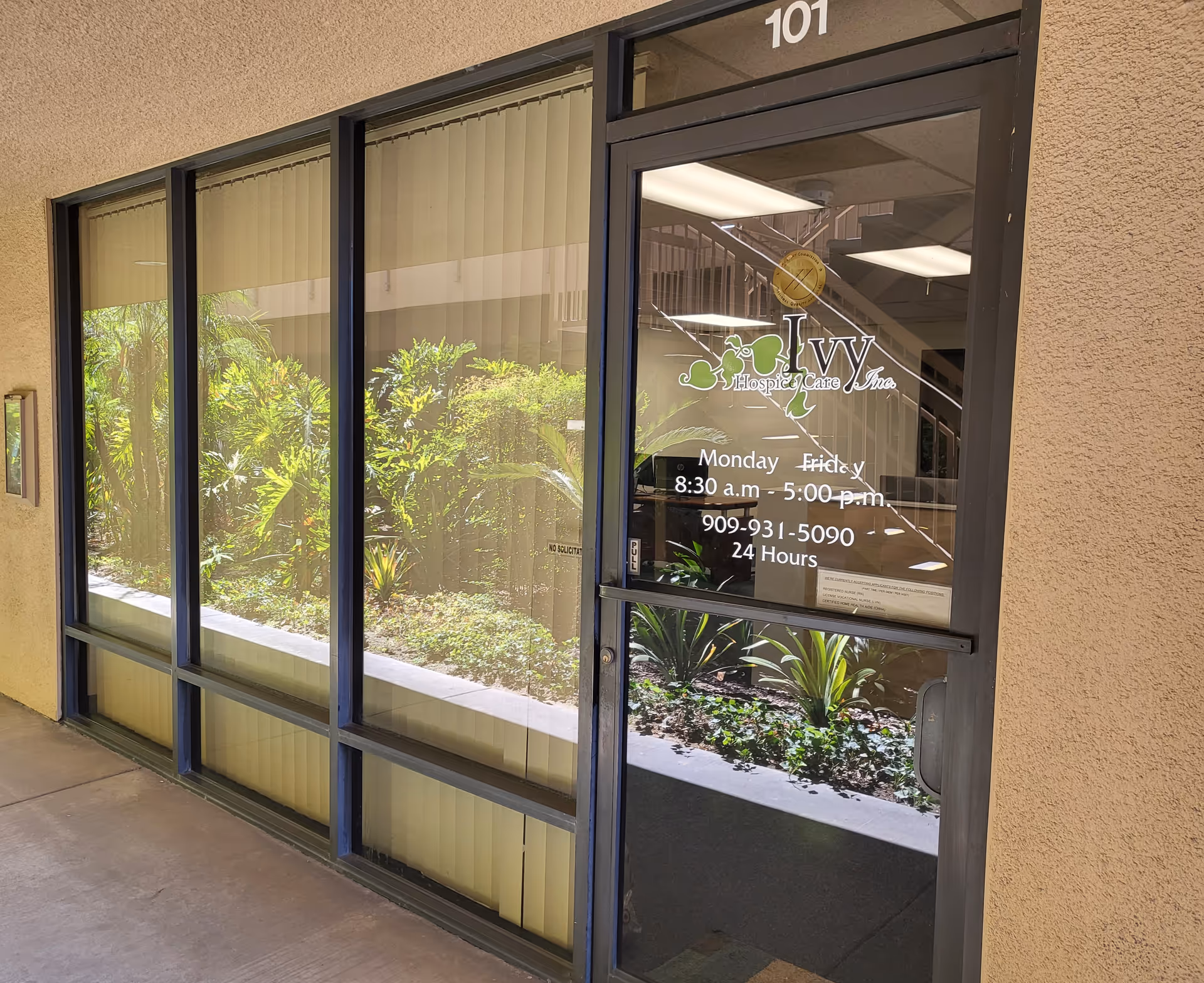 Front entrance to Ivy Hospice Care with glass door and logo, landscaping outside.