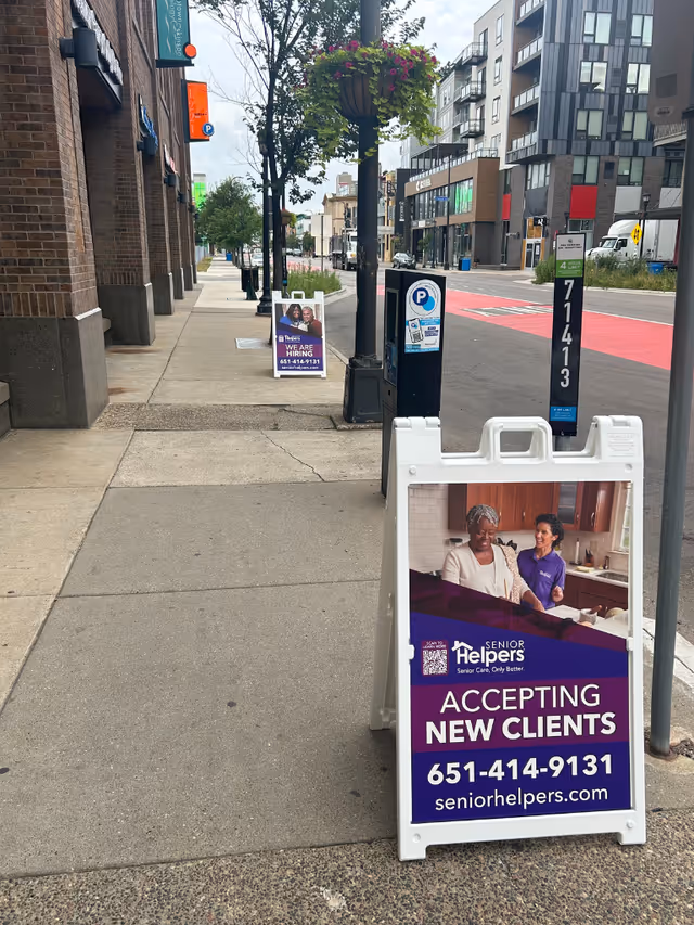 Outdoor urban sidewalk with a Senior Helpers sign advertising accepting new clients.