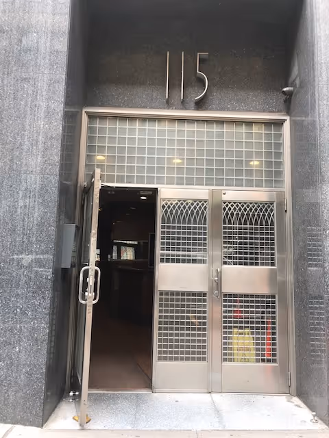 Exterior building entrance with metal double doors and security grilles, numbered 115.