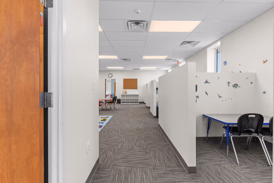 Bright hallway with white partition cubicles and small desks in a senior living space.