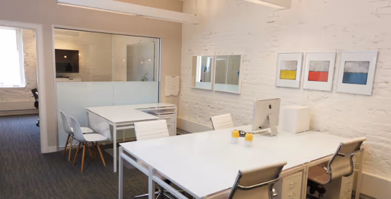 Bright modern office area with white desks, chairs, computer, glass partition, and brick accent wall.