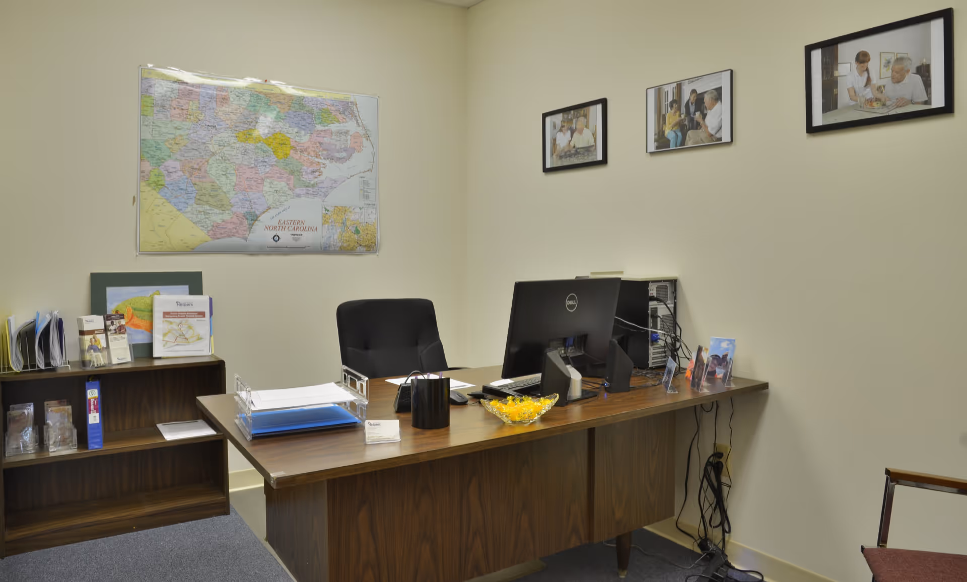 An office workspace featuring a desk, computer, map, and framed photos.