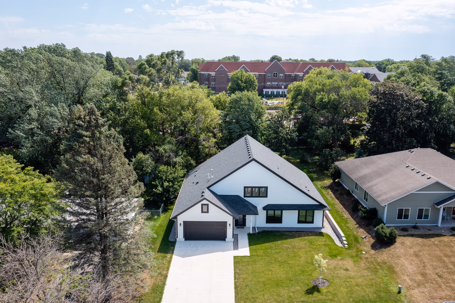 Aerial view of a modern white house with a black roof and driveway.