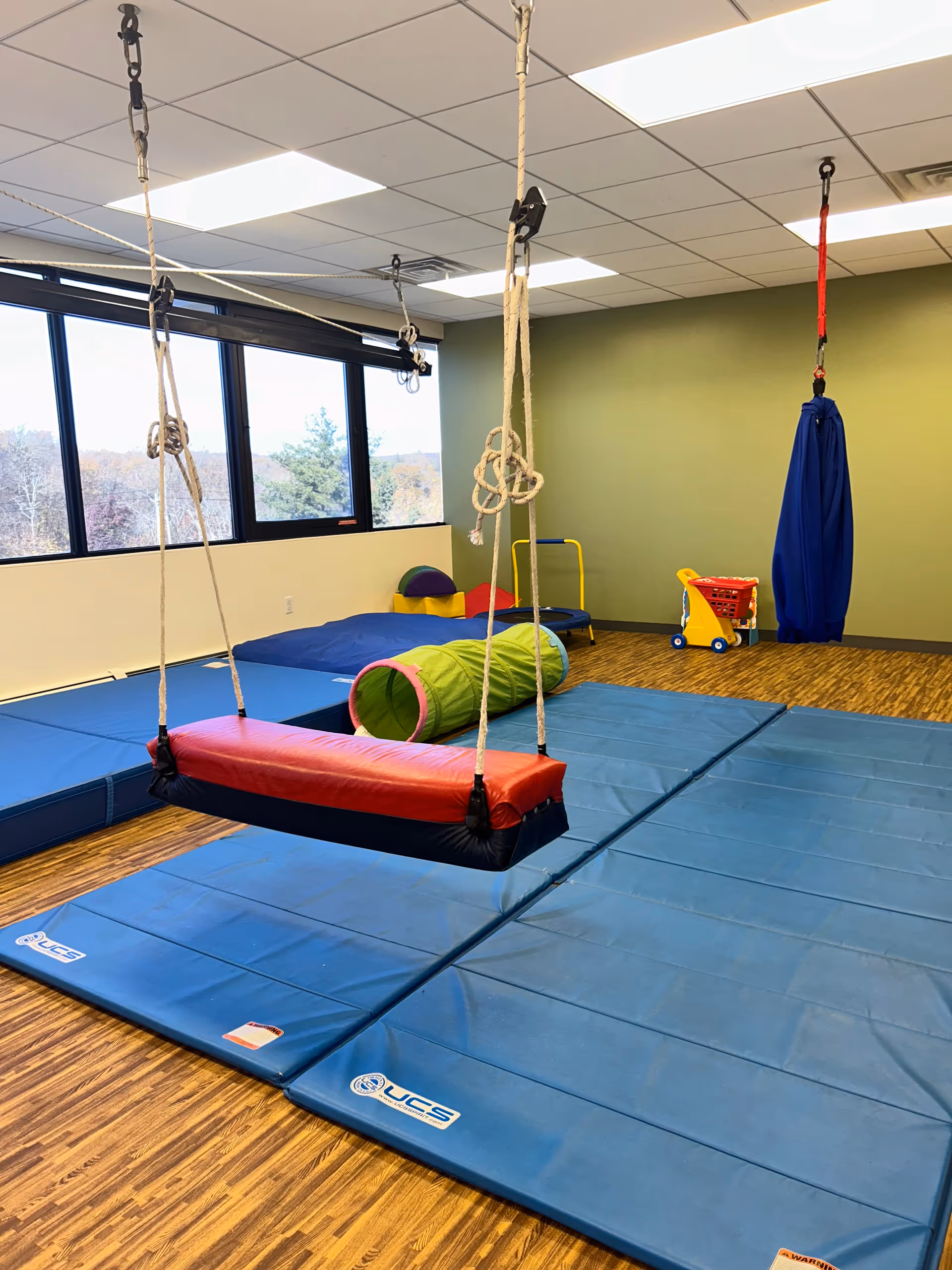 Indoor sensory gym with padded blue mats, climbing ropes, and soft play equipment.