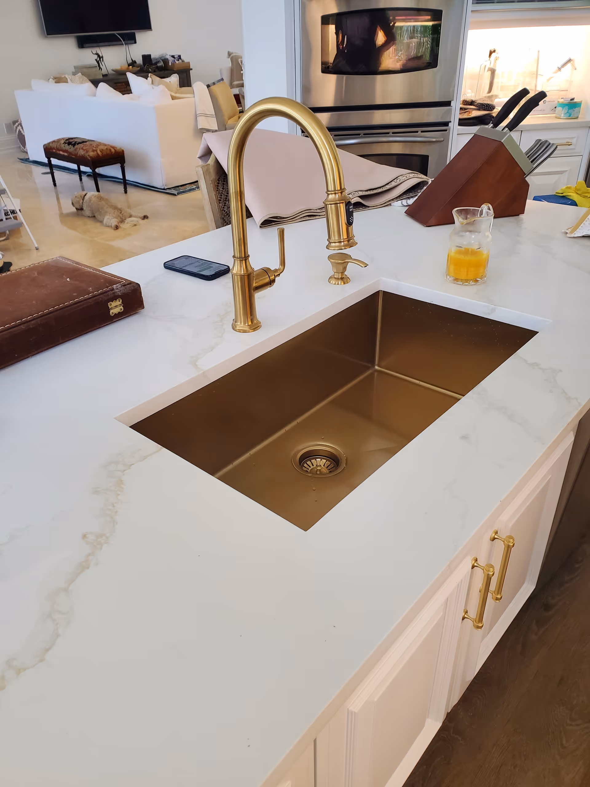 Brass kitchen sink with a gold faucet on a marble island in a modern kitchen.