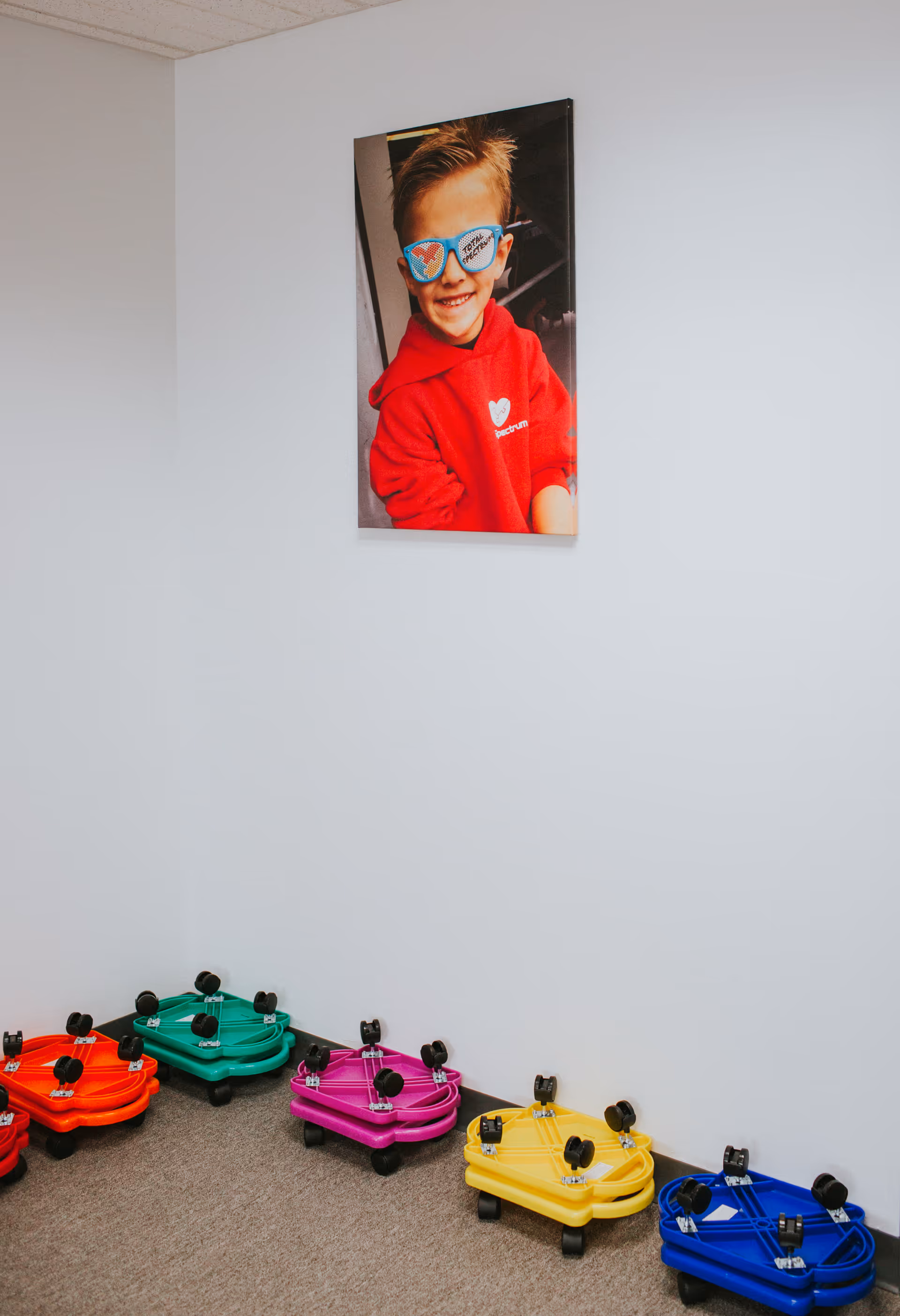 White room with a poster of a child and colorful wheeled toys on the floor.