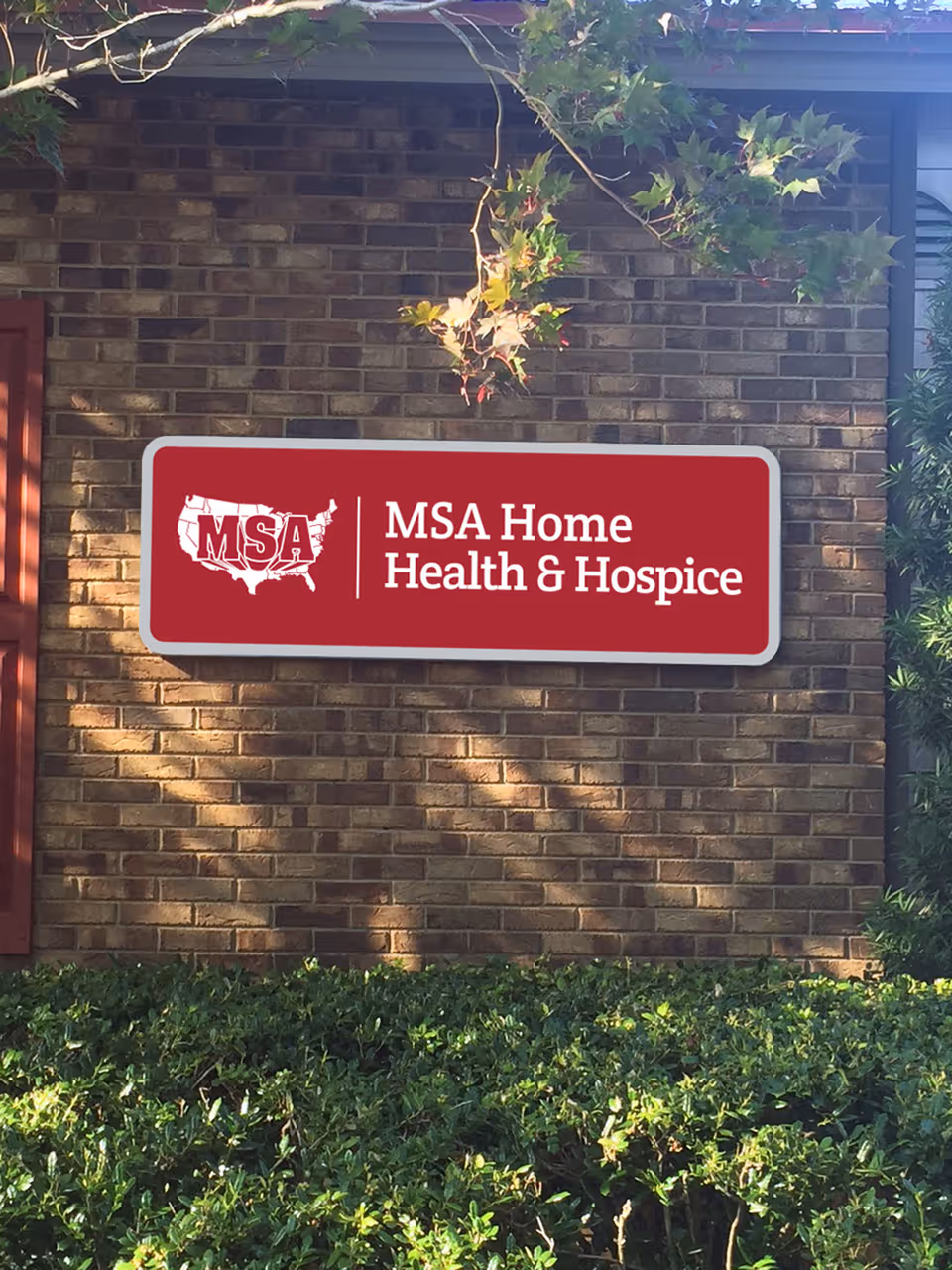 Red MSA Home Health & Hospice sign mounted on brick exterior wall with foliage