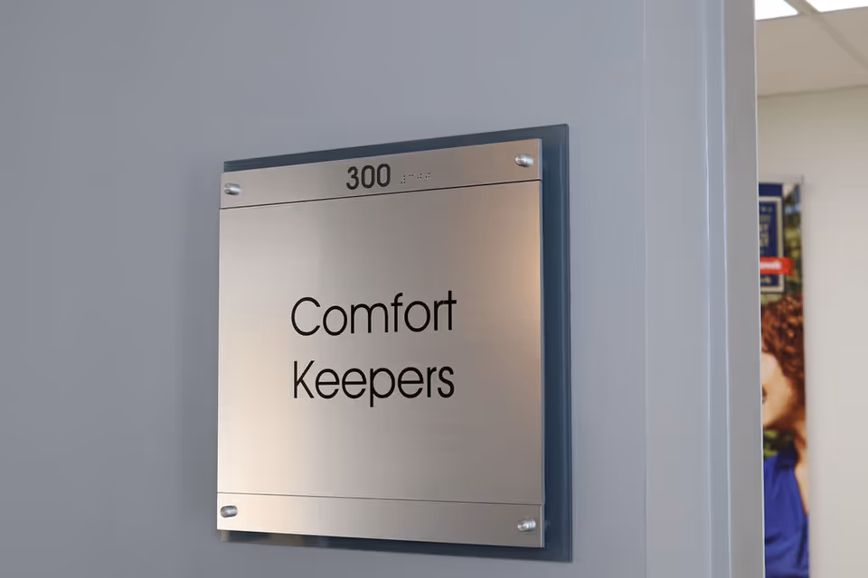 Metal plaque on a blue wall reads Comfort Keepers and room 300