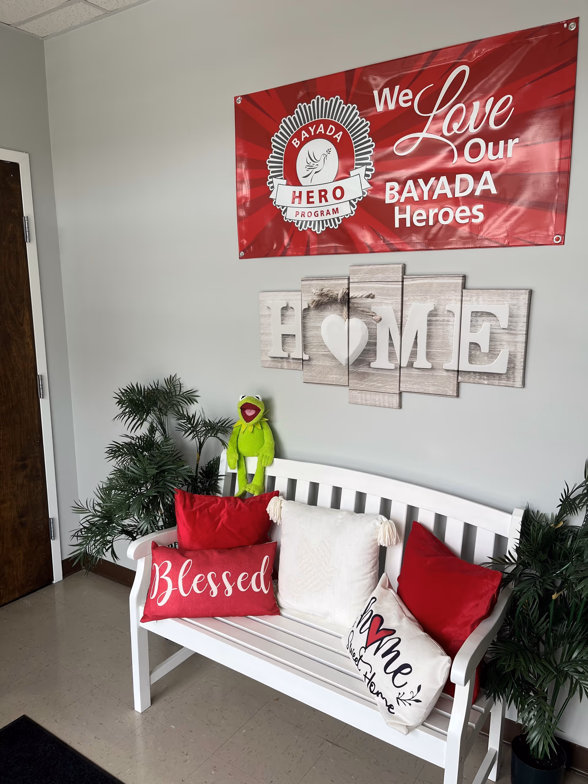 White bench with red cushions, plants, and a BAYADA banner in a cozy waiting area.