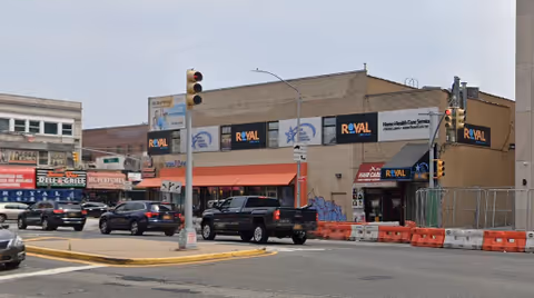 Exterior street view of a Royal Care facility with construction barriers and parked cars.