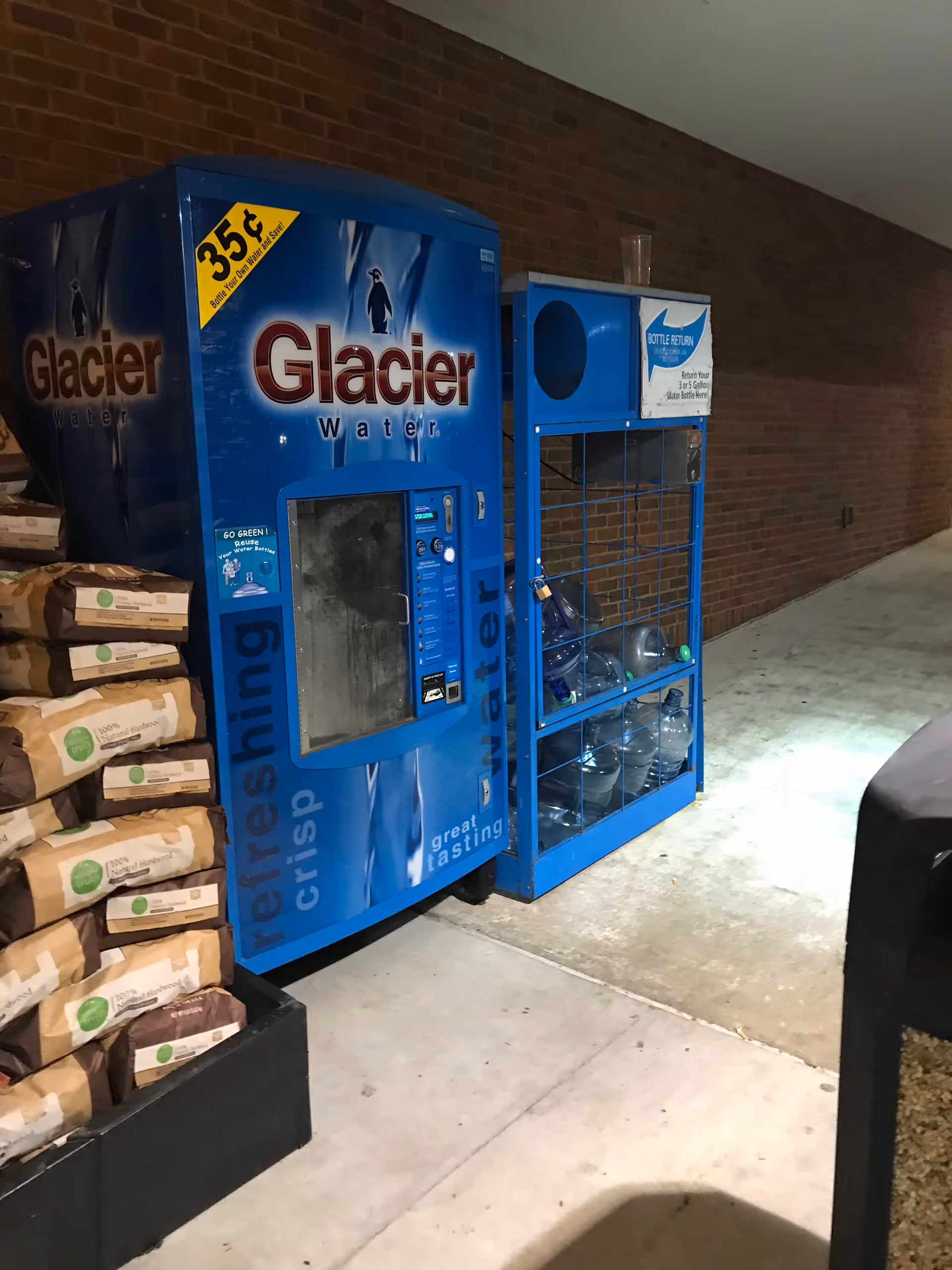 Two blue Glacier water vending machines in a brick-walled hallway.