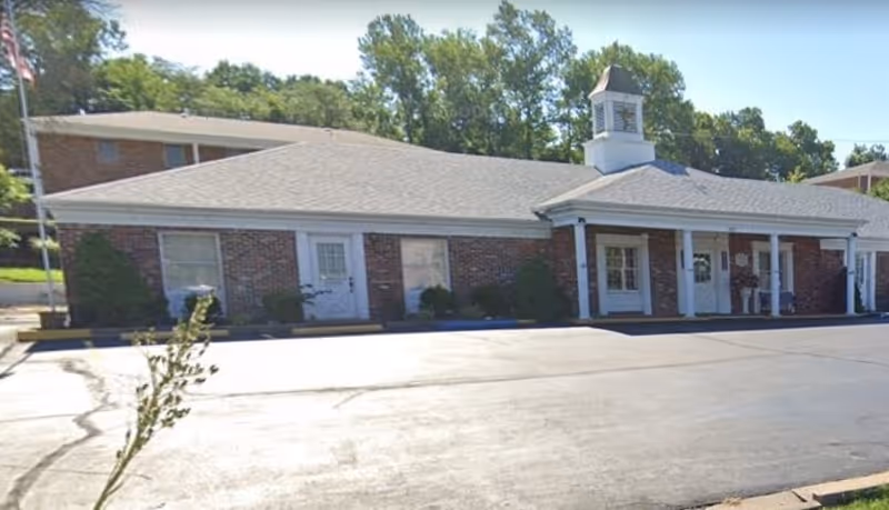 Brick senior living facility exterior with a front entrance, white columns, and a cupola.