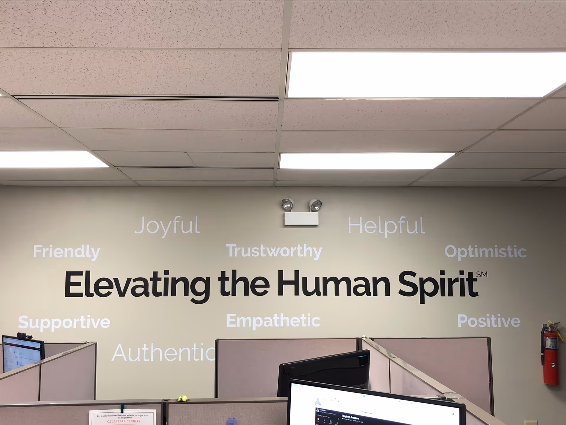 Office interior with cubicles and a wall displaying inspirational words around Elevating the Human Spirit.