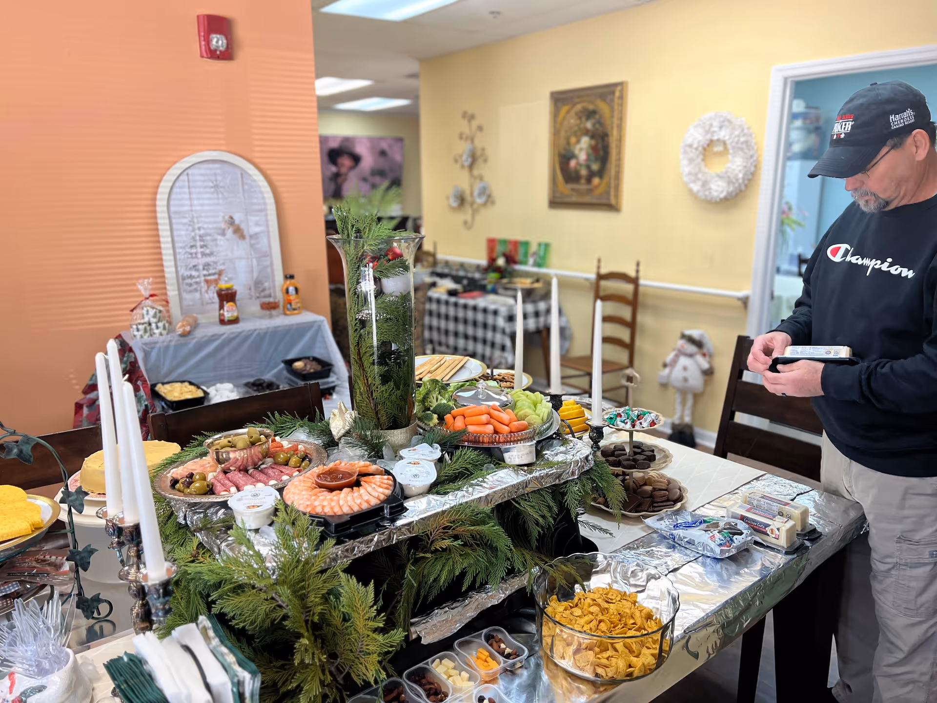 Buffet-style food spread on a decorated table in a dining area with a man nearby.