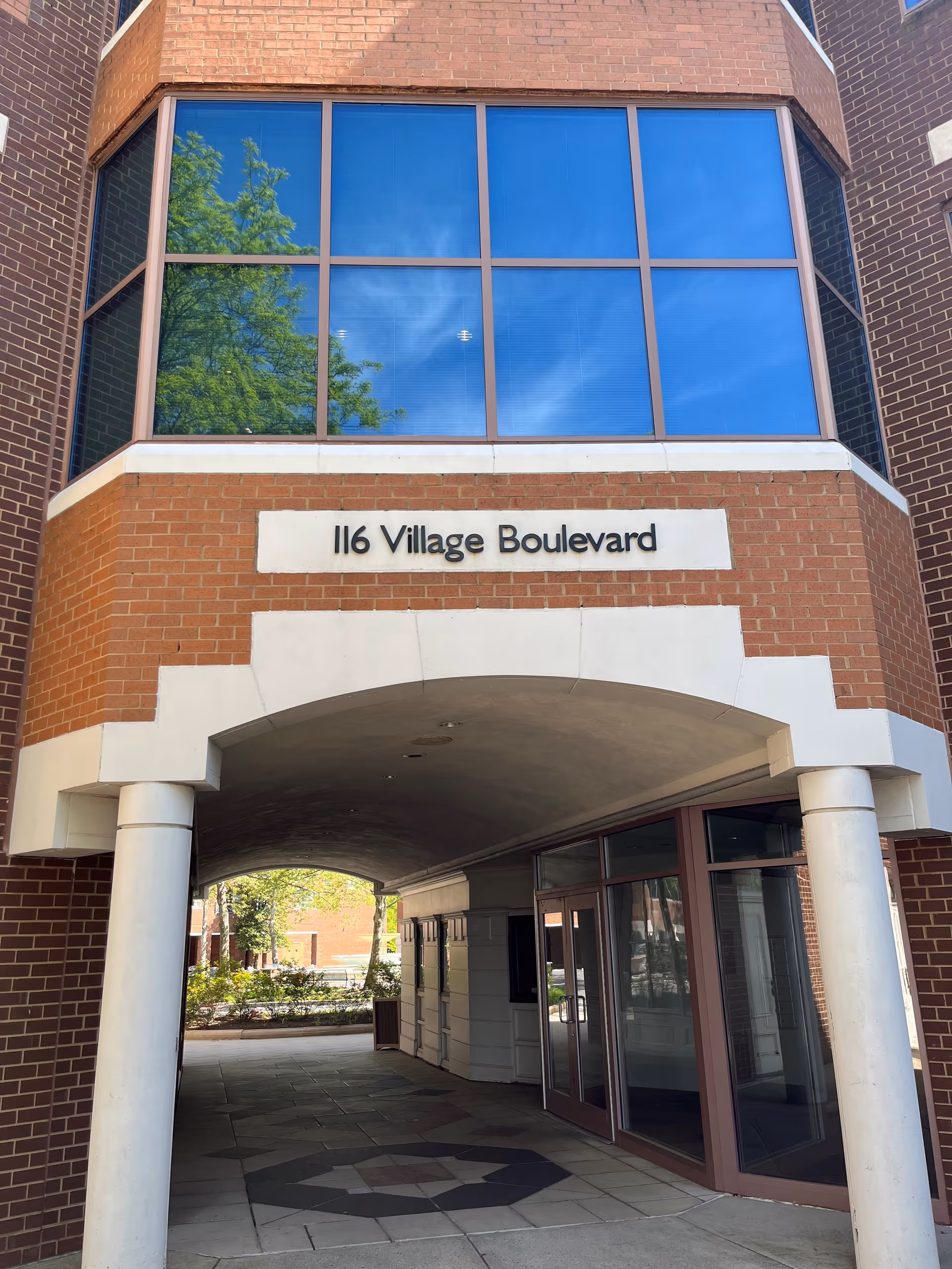 Brick building entrance with large glass windows and a sign reading '116 Village Boulevard'.