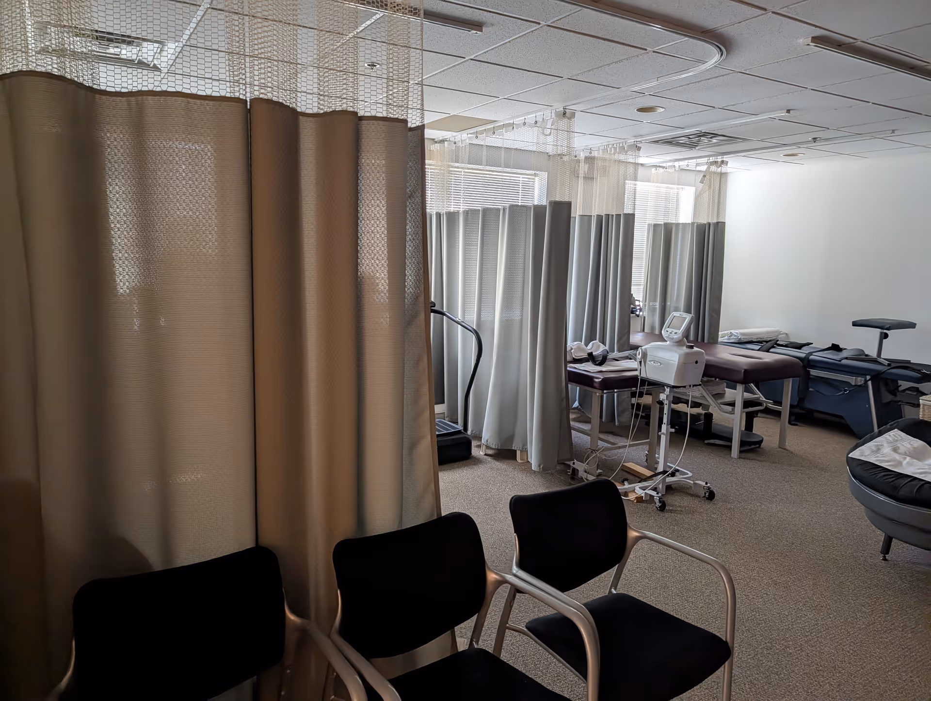 Clinic treatment area with privacy curtains, medical beds, and chairs in a wound care setting.