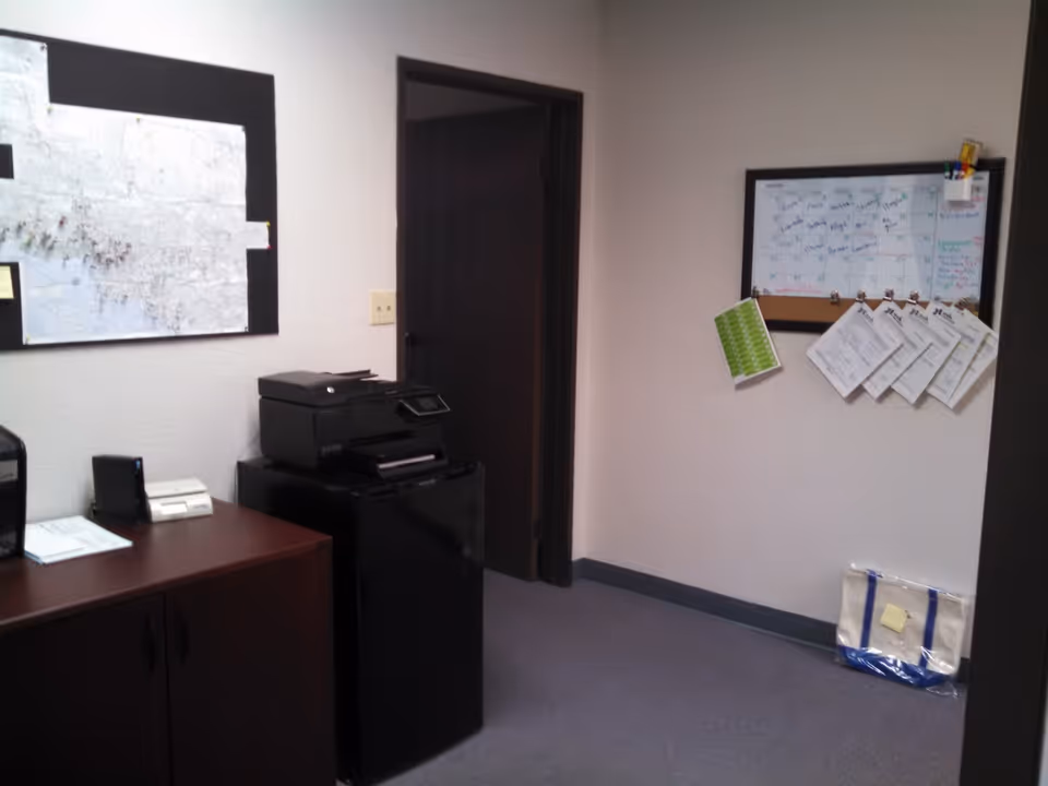 Office area with printer, map, calendar, and wall-mounted documents on beige walls.