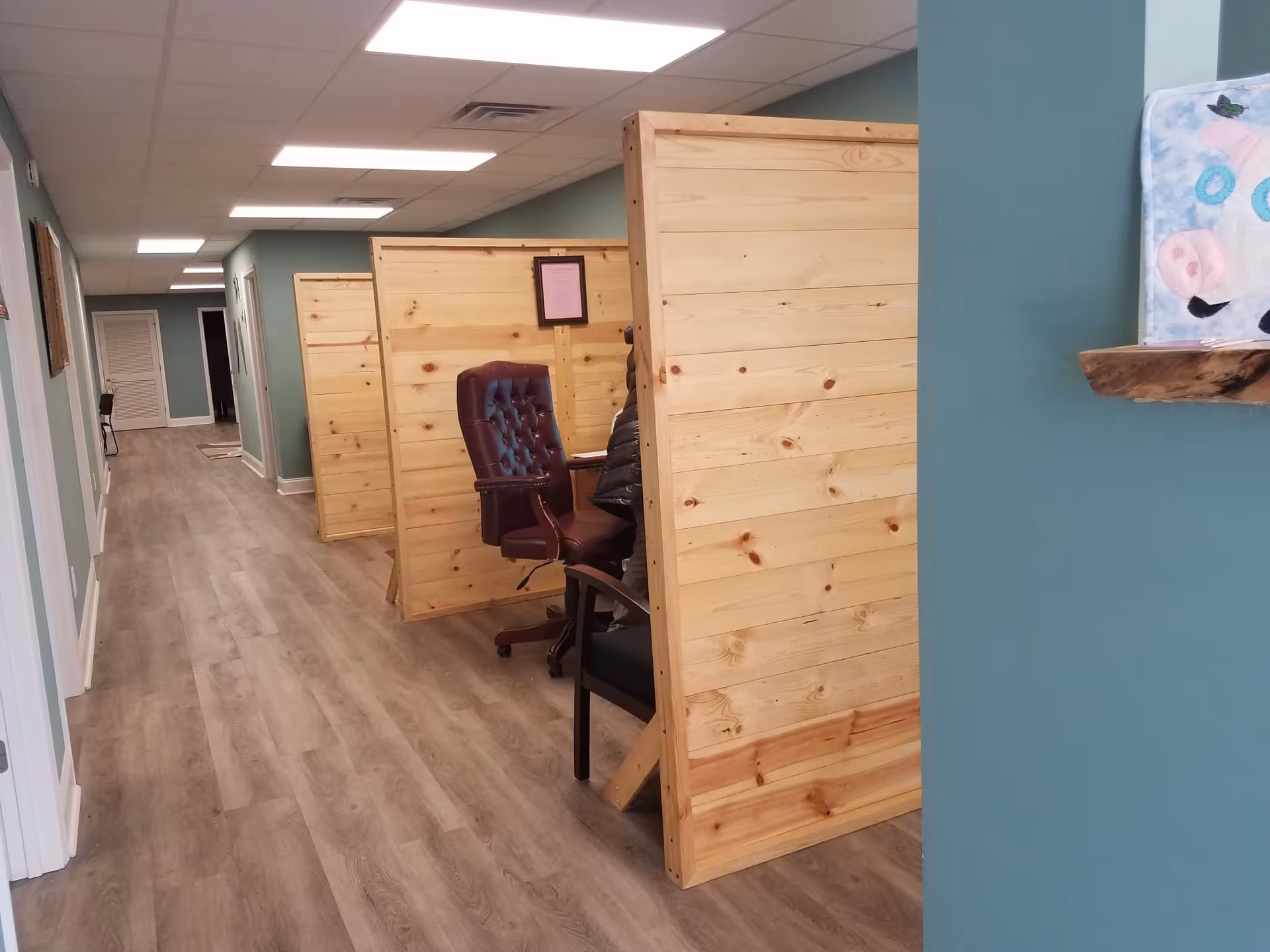 Long hallway with wooden privacy panels and office chairs inside a senior home care facility.