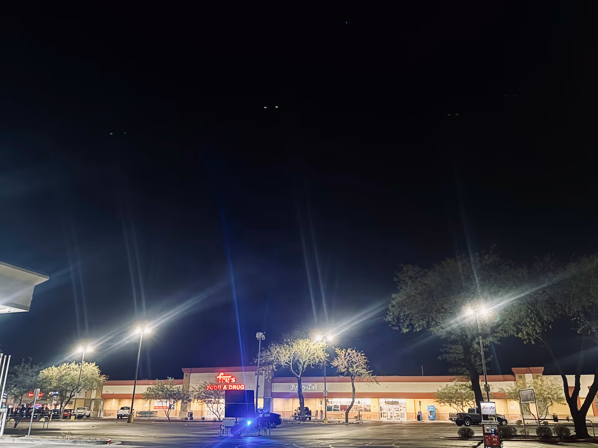 Night exterior of a strip mall with bright parking-lot lights and storefronts.