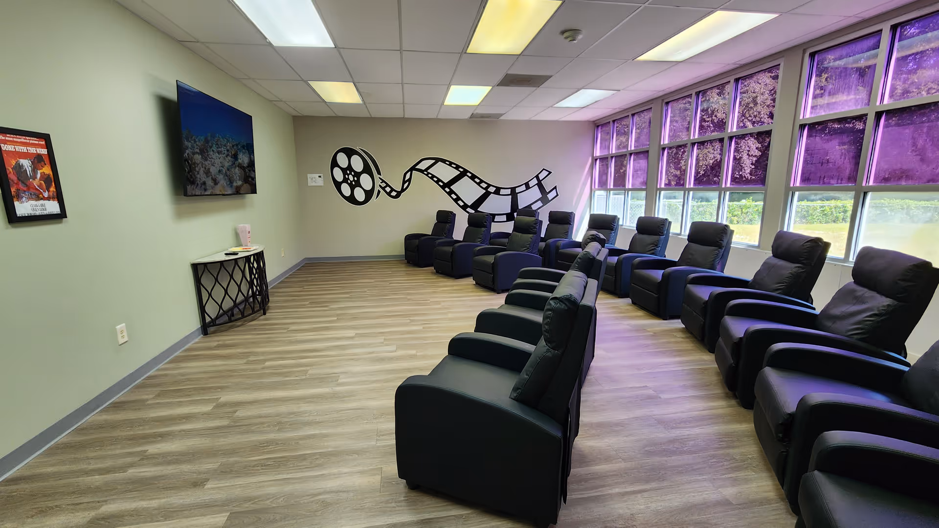 Spacious lounge with rows of black recliners and a film reel wall mural.