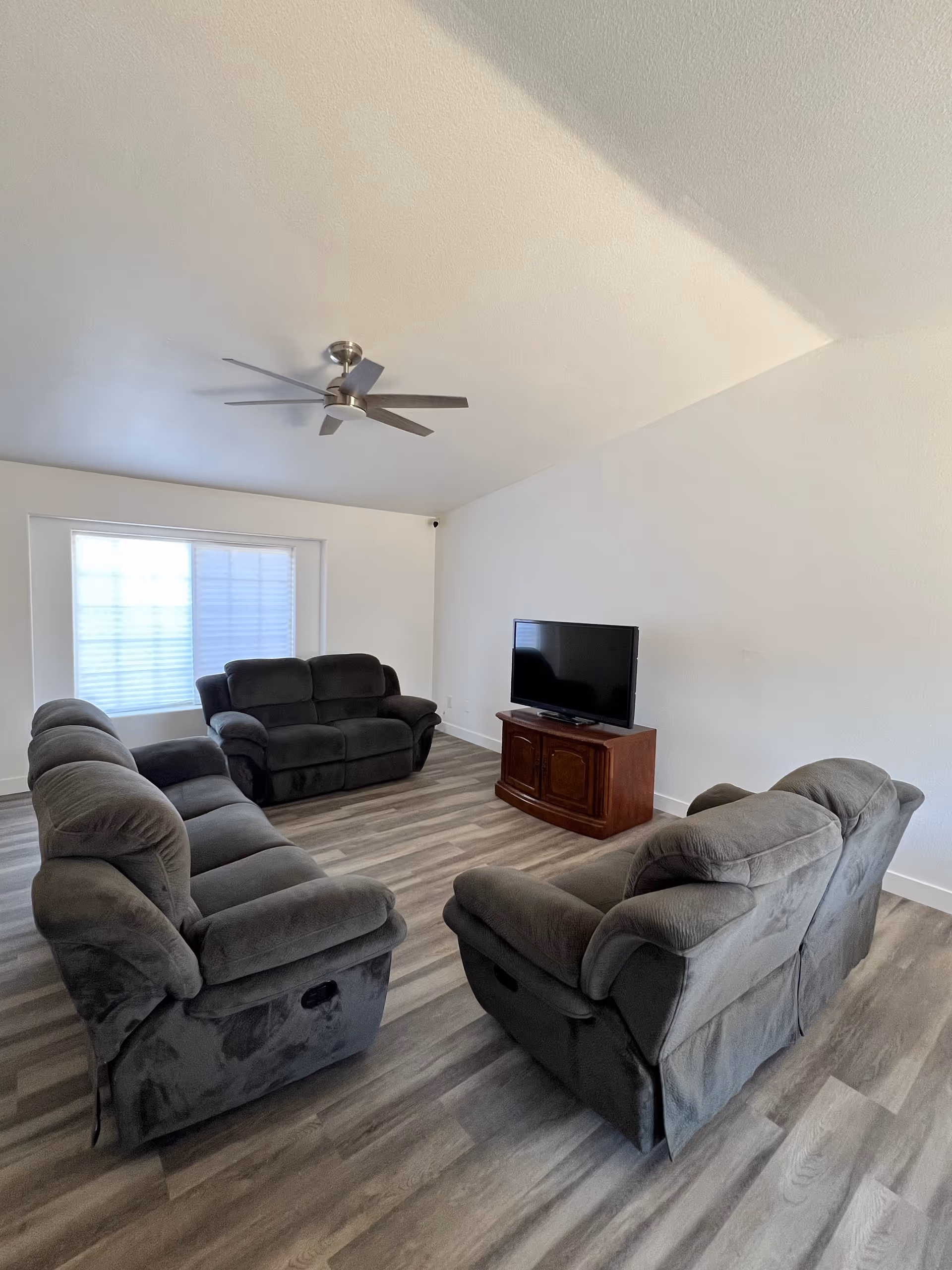 Spacious living room with gray recliner sofas and a TV on a wooden stand.
