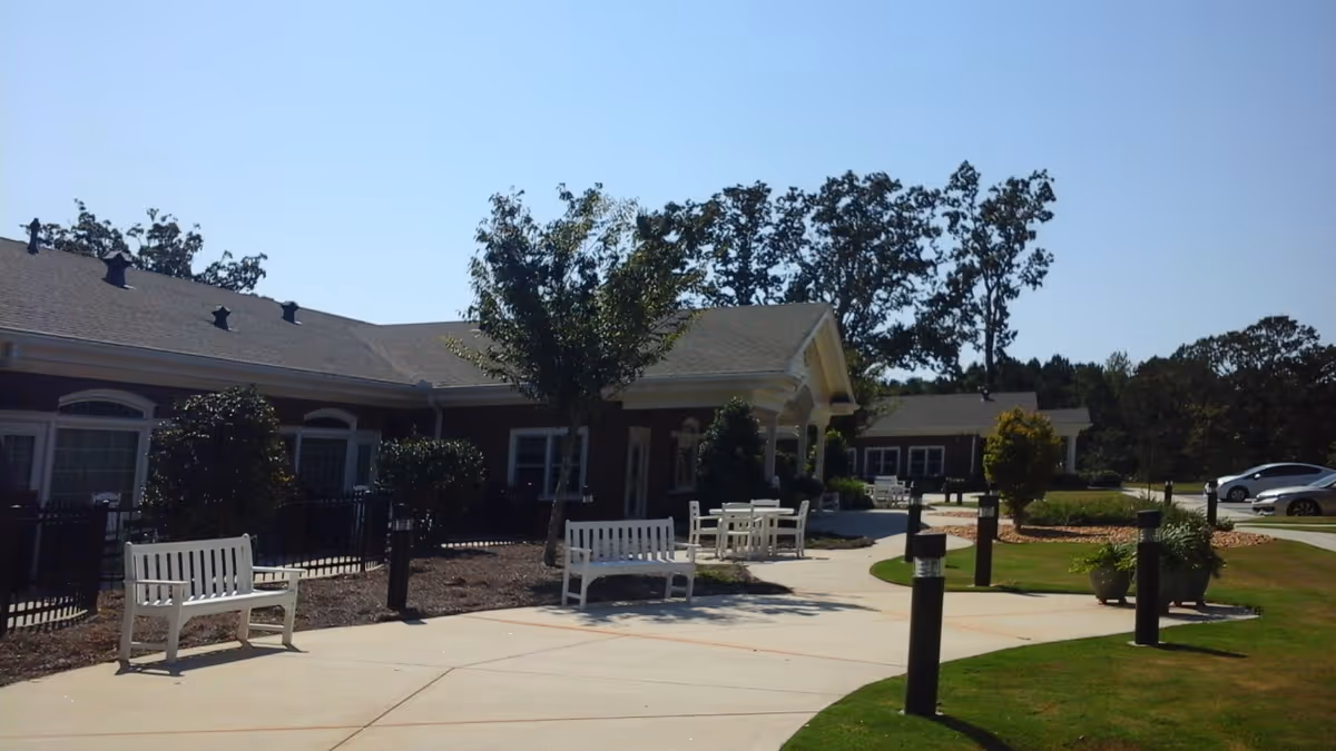 Sunny outdoor courtyard with white benches and a walkway beside a single-story hospice facility.