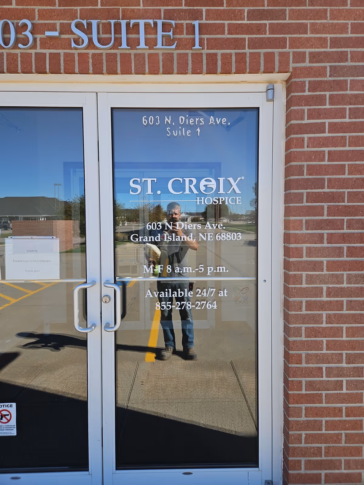 Brick exterior entrance with glass doors labeled St. Croix Hospice, reflecting a person taking photo.