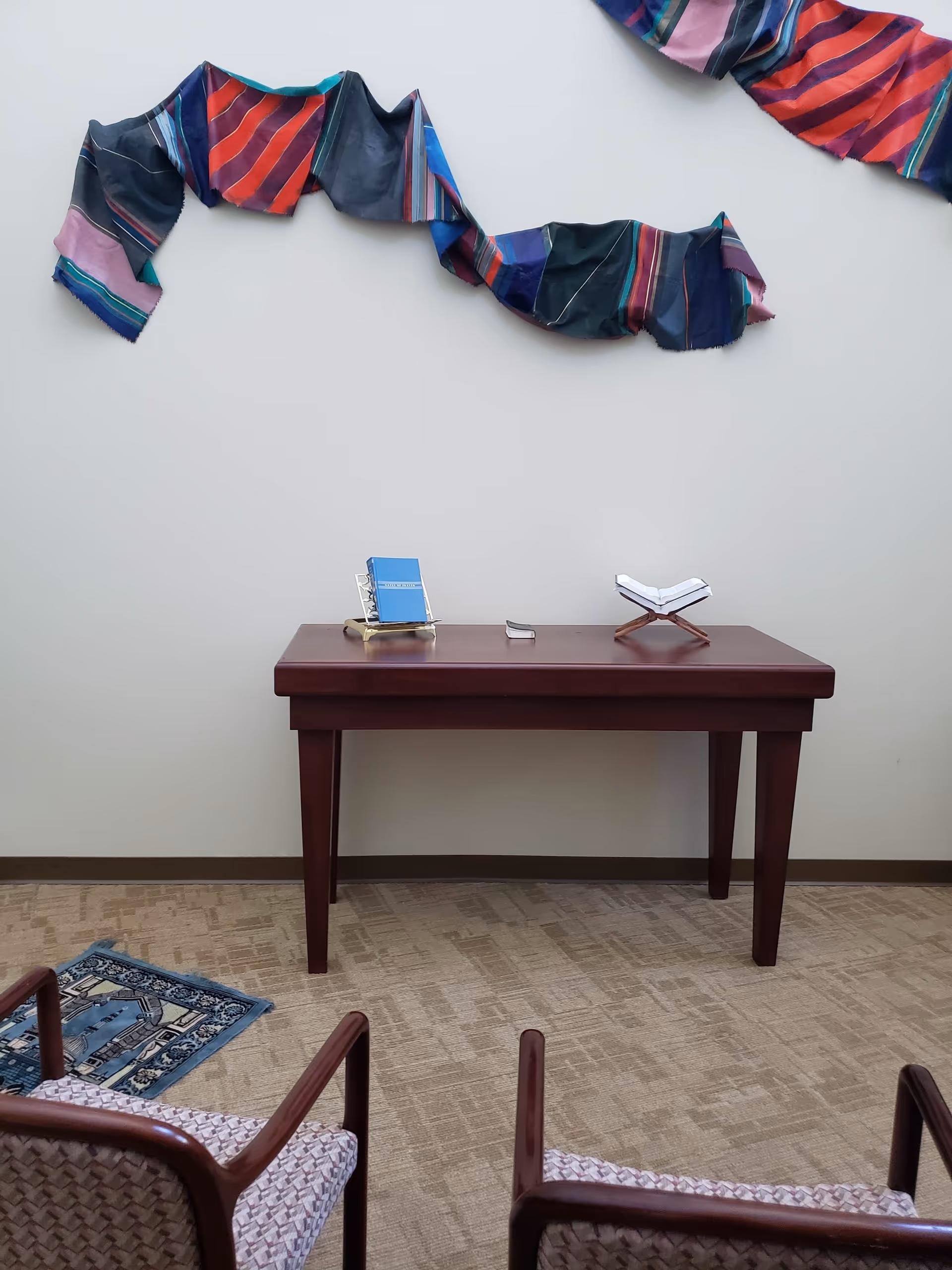 A wooden desk with reading materials sits in a waiting area, colorful fabric art overhead.