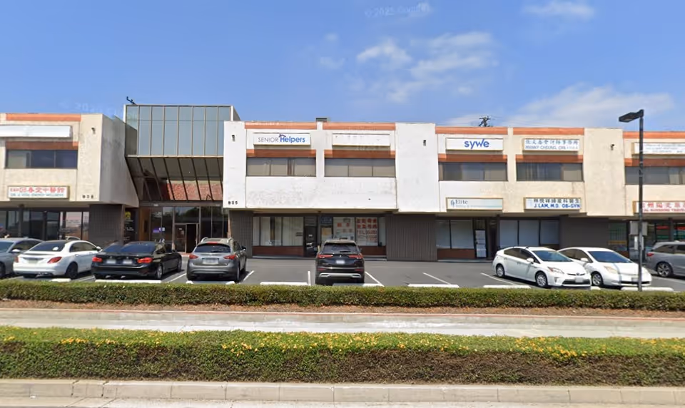 Exterior view of a strip mall with a Senior Helpers sign and parked cars.