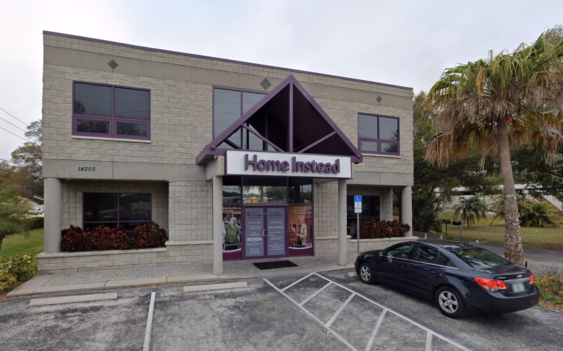 Front exterior of a Home Instead building with a purple-framed entrance and parked car.