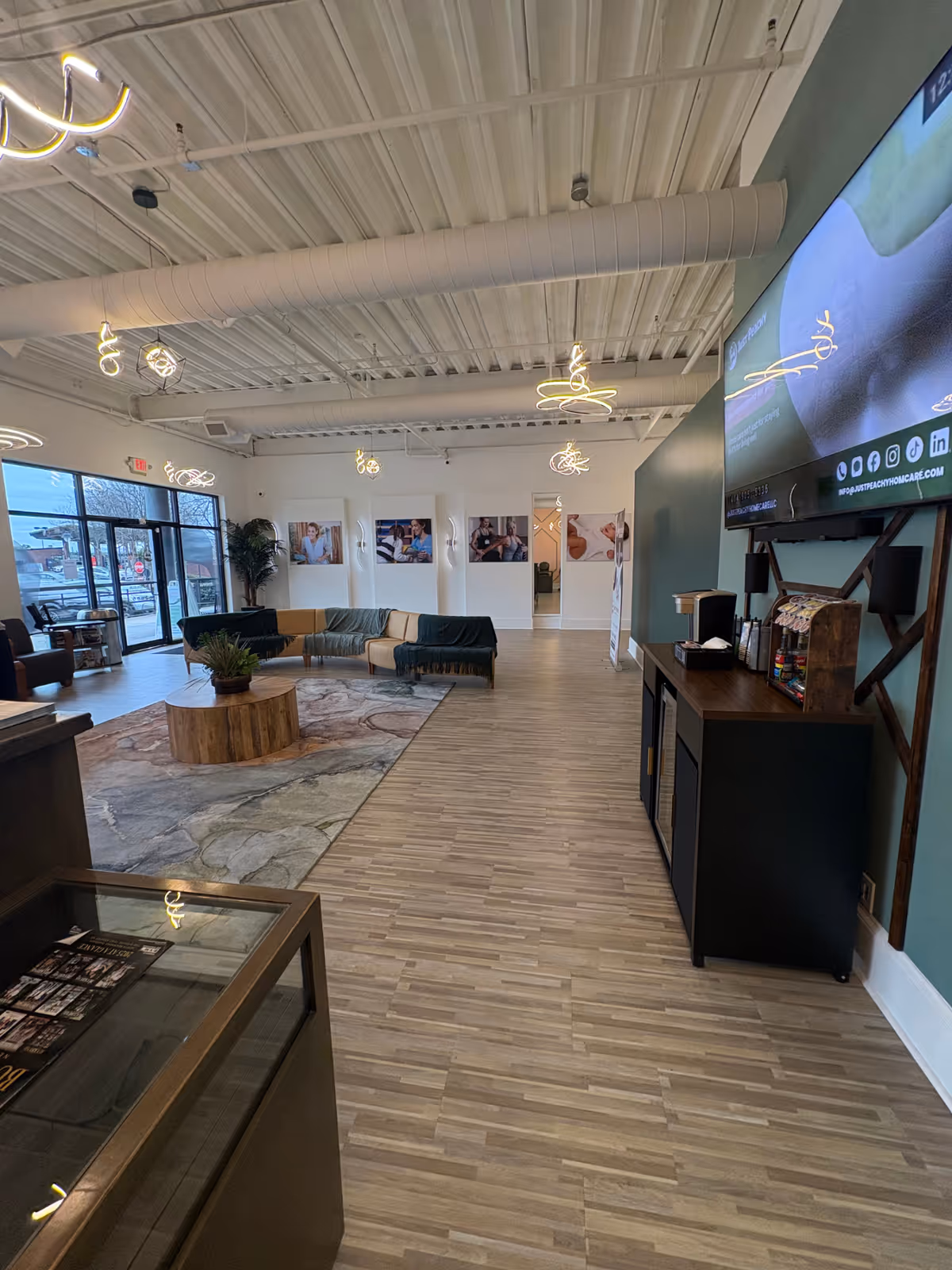 Modern senior living lobby with sofas, coffee table, plants, rug, and a large wall TV.