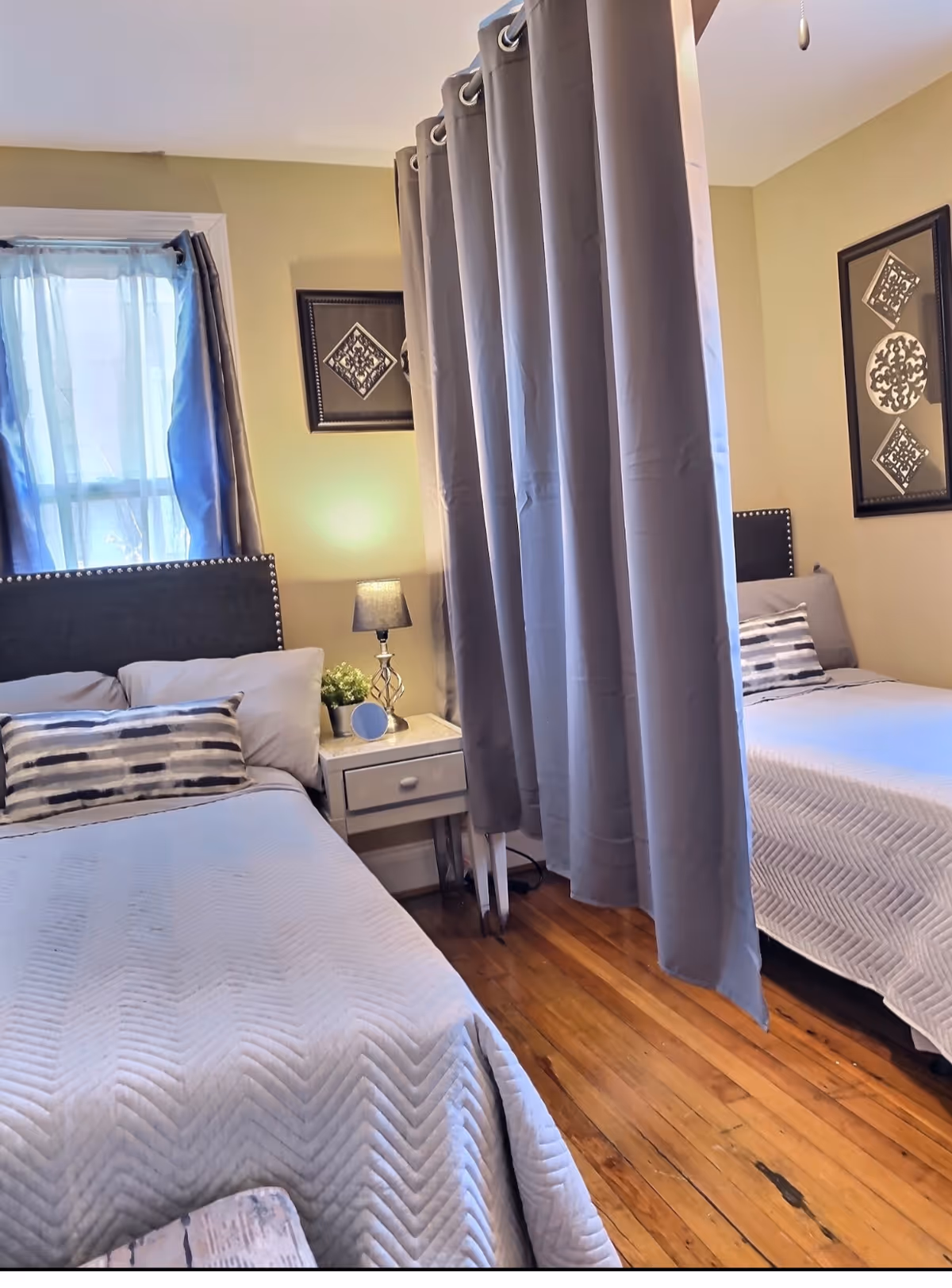 Two twin beds with gray quilts sit beside a shared nightstand in a cozy bedroom.