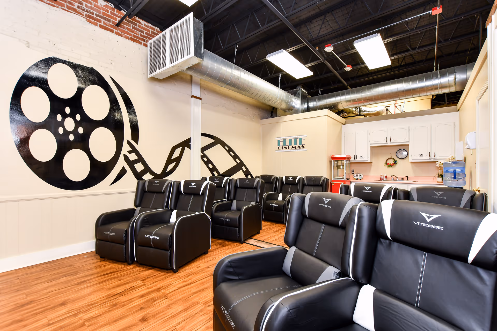 A spacious senior living lounge with black leather cinema chairs and a film reel mural.