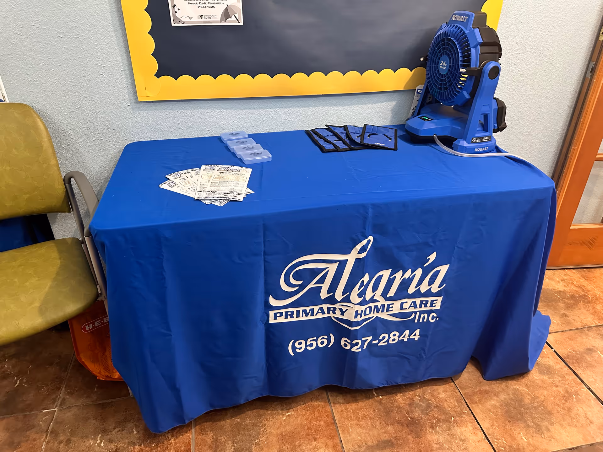 Blue table with Alegria Primary Home Care branding and a blue fan on the table.
