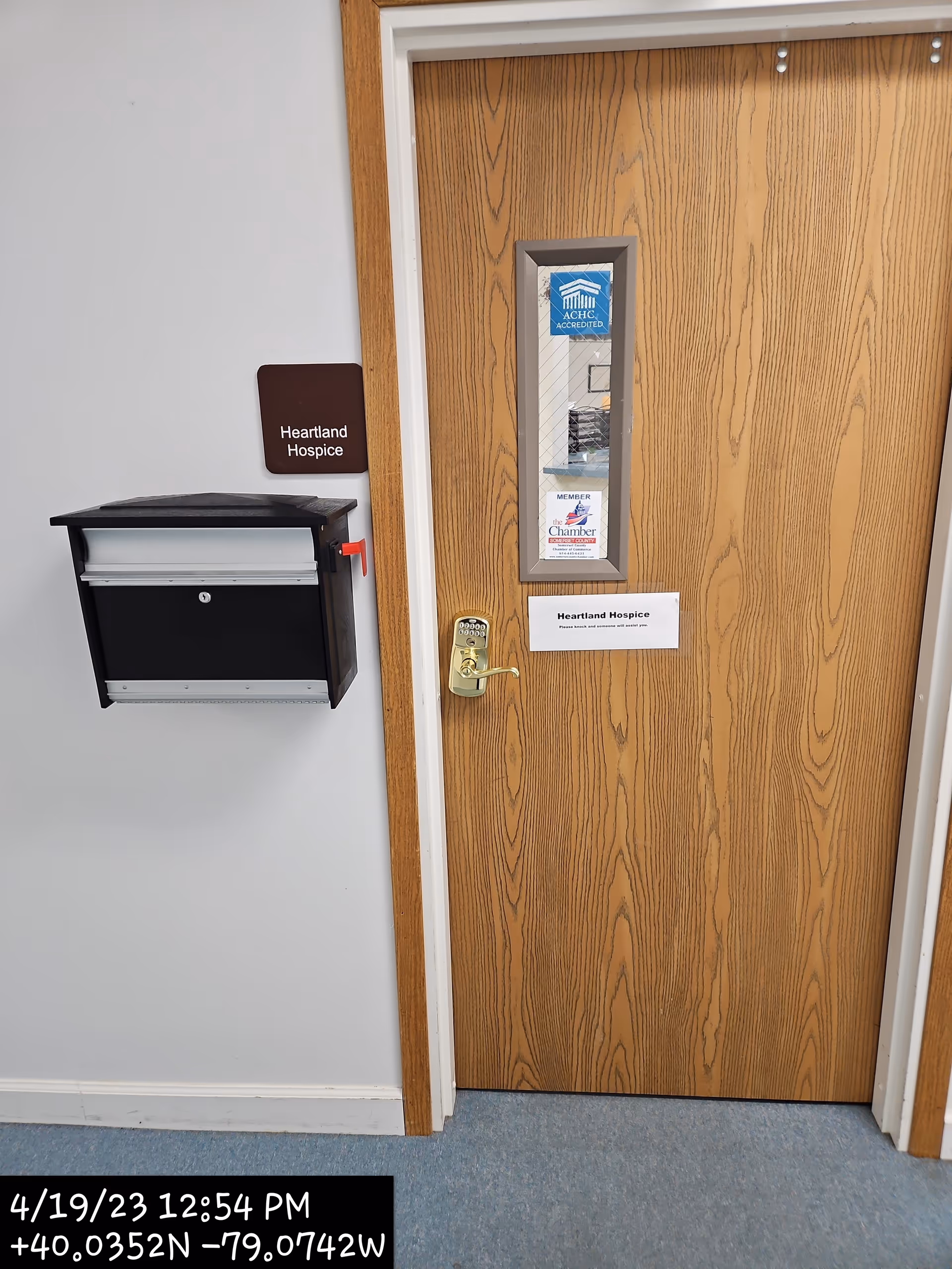 Wooden door labeled Heartland Hospice in a hallway with a mailbox and notices.