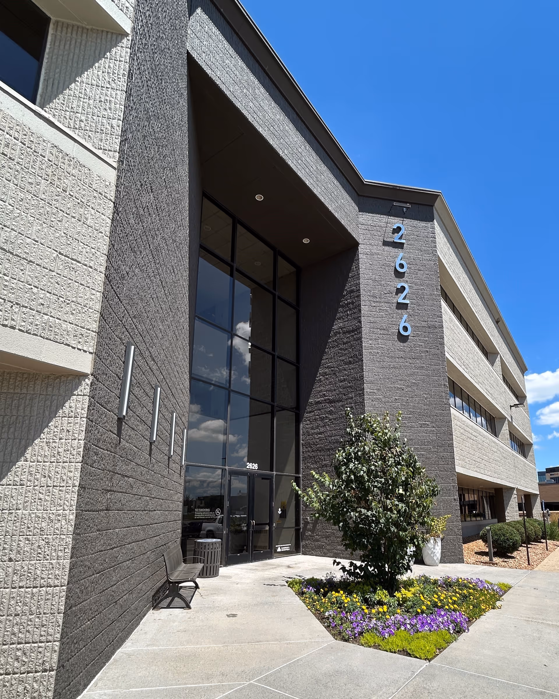 Modern senior living facility entrance with tall glass doors, brick facade, and landscaped front.